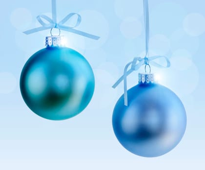 Two Christmas decorations hanging on ribbons with blue background