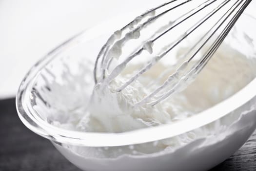 Closeup of metal whisk whipping cream in glass bowl