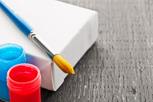 Paintbrush on white blank canvas with red and blue paints