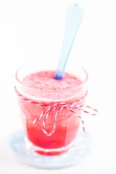 Closeup of strawberry smoothie and blue plastic spoon in glass on light blue plate