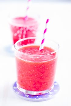 Closeup of strawberry smoothie and striped straw in glass on purple plate with another in background