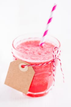 Closeup of strawberry smoothie and purple striped straw in glass with cardboard tag on light background