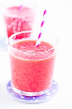 Closeup of strawberry smoothie and striped straw in glass on purple plate with another in background