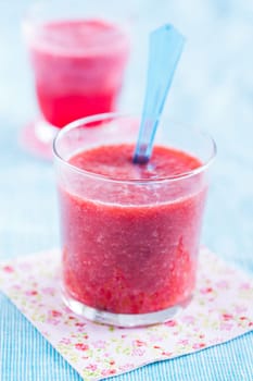 Closeup of strawberry smoothie in glass resting on floral serviette on light blue tablecloth with another in background