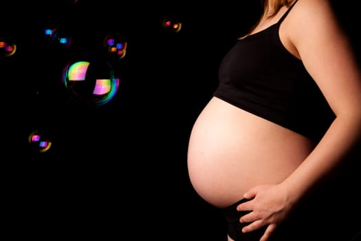 Belly of pregnant woman with soap bubbles. Monochrome and color mix. Black background