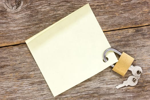 Padlock with empty  sticky note on the wooden background