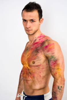 Muscular young man shirtless with skin painted with Holi colors, looking at camera