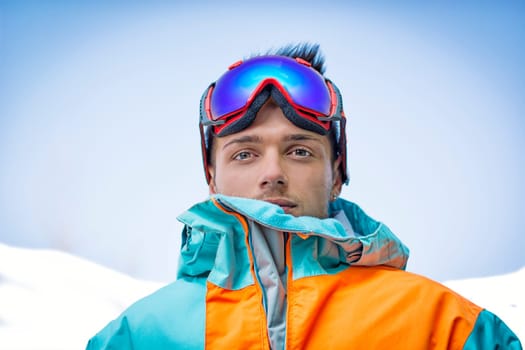 Friendly attractive skier or snowboarder against blue sky looking at camera
