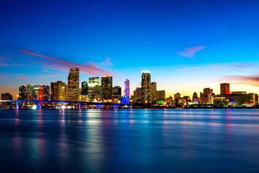 Miami city skyline panorama at dusk with urban skyscrapers over sea with reflection