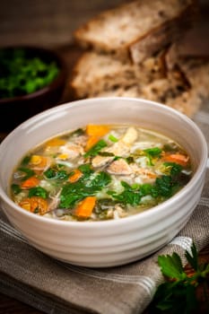 Chicken rice soup with vegetables in bowl and bread on rustic table