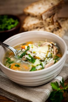 Chicken rice soup with vegetables in bowl and bread on rustic table
