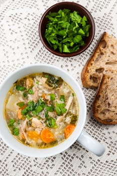 Cup of hot chicken rice soup served with bread and parsley from above on crochet tablecloth