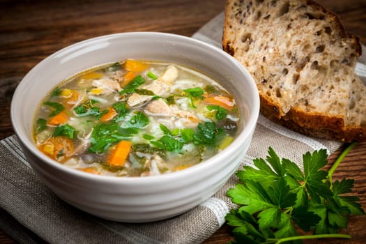 Chicken rice soup with vegetables in bowl and bread on rustic table