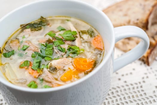 Cup of hot chicken rice soup served with bread on crochet tablecloth closeup