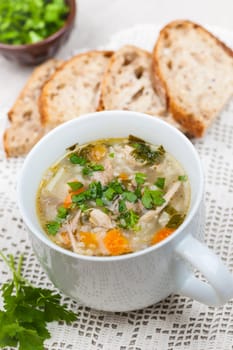 Cup of hot chicken rice soup served with bread and parsley on crochet tablecloth