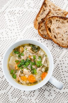Cup of hot chicken rice soup served with bread from above on crochet tablecloth