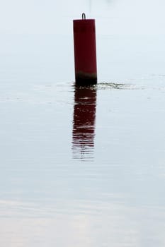 The photograph of a red buoy on a calm surface of water in the backlight.