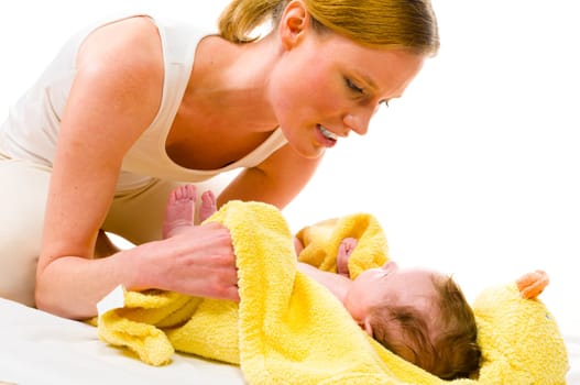 Adult mother wearing bright casual clothes, she kneels on the floor and dries the freshly bathed newborn baby with a yellow towel and smiling while doing. Isolated against white background.
