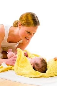 Adult mother wearing bright casual clothes, she kneels on the floor and dries the freshly bathed newborn baby with a yellow towel and smiling while doing. Isolated against white background.