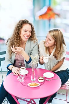 Two smiling women meeting for coffee in cafe and laughing