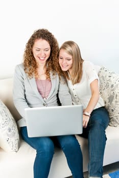 Two young smiling women using laptop computer at home