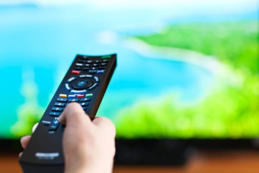 Hand holding television remote control pressing buttons