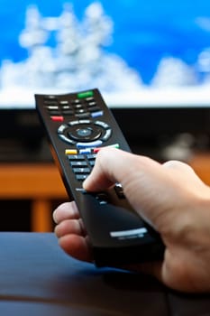 Hand holding television remote control pressing buttons