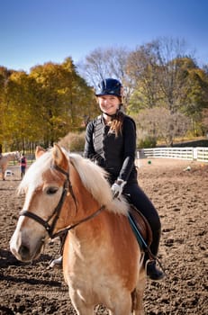 Portrait of teenage girl riding horse outdoors on sunny autumn day