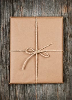 Gift package in brown paper wrapper tied with string on rustic wood background