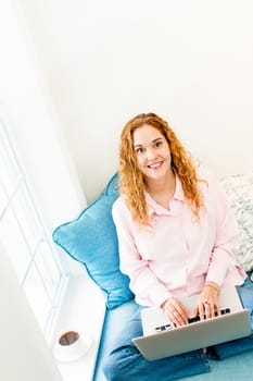 Caucasian woman with laptop computer looking up sitting on couch at home