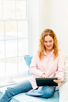 Smiling caucasian woman using tablet computer at home by window