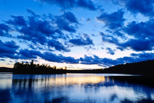 Sun setting over tranquil lake and forest in Algonquin Park, Canada