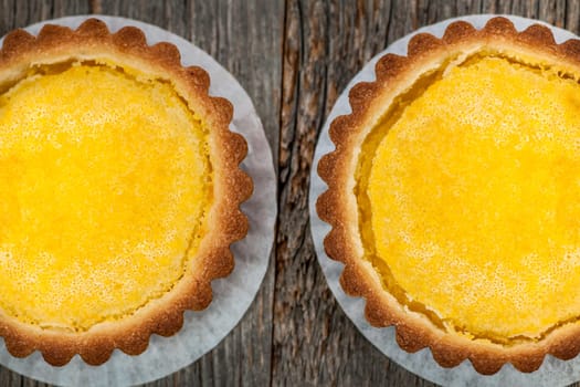 Two fresh gourmet lemon dessert tarts on wood background from above
