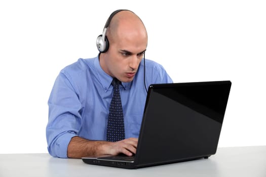 Businessman wearing headphones typing on laptop