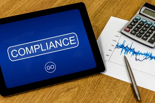 compliance word on digital tablet with calculator and financial graph