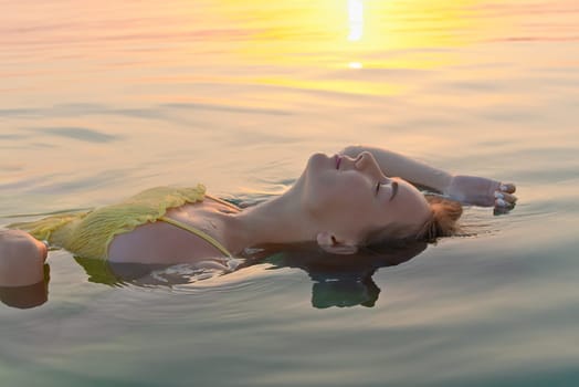 Beautiful young woman relaxes in the morning on sea water in the sun, swims and relaxes.