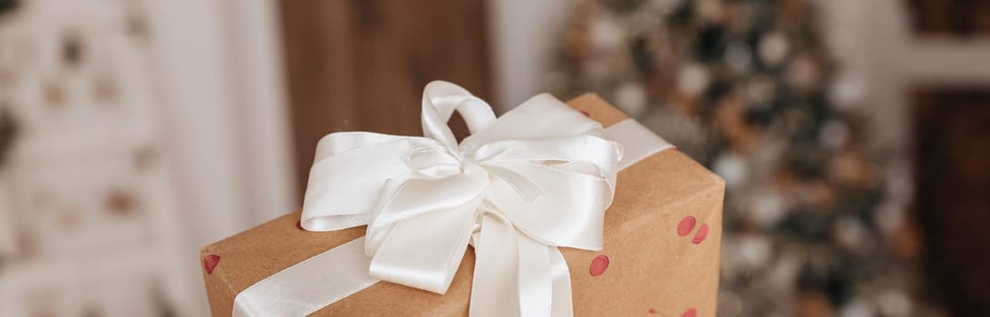 Wrapped in golden paper present boxes on table closeup and veautiful holdiay decorated christmas tree with ornaments and garland unfocused. Winter holiday background