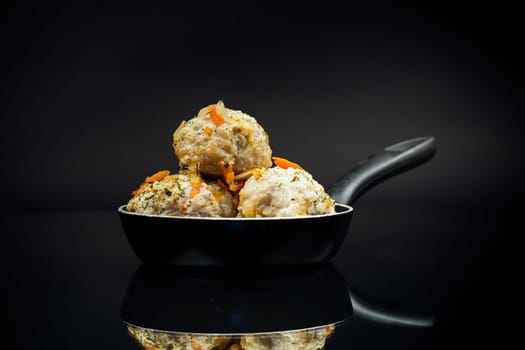 cooked chicken diet meatballs in a frying pan, isolated on a black background