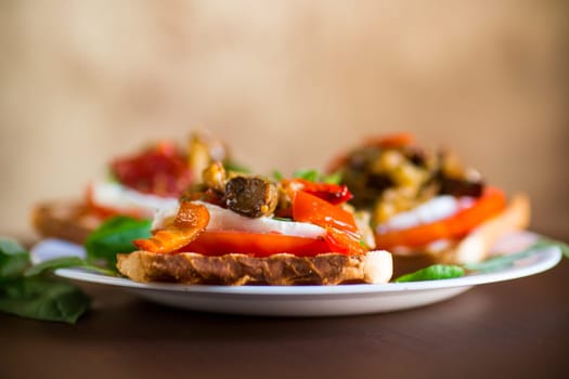 Prepared sandwich with tomatoes, mozzarella and fried eggplant with mushrooms in a plate on a wooden table.