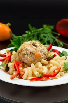 cooked pasta with meatballs, peppers and herbs with spices in a plate, isolated on a black background