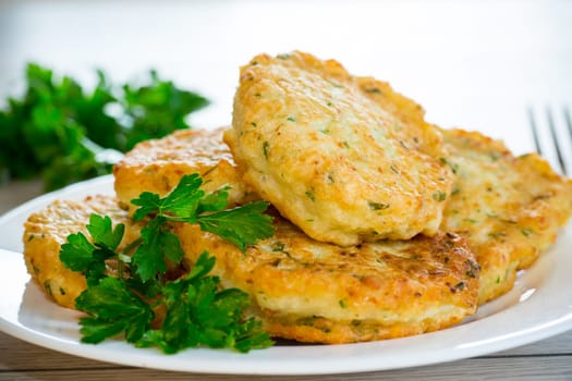 cooked fried potato cutlets with herbs, in a plate on a wooden table.