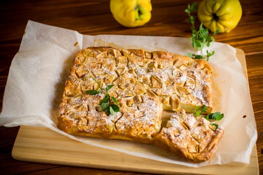 prepared curd semolina pie with quince inside and covered with powdered sugar on a wooden board.