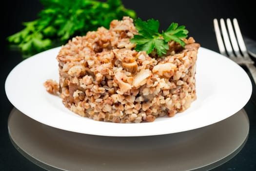 cooked buckwheat boiled with mushroom filling in a plate isolated on a black background.