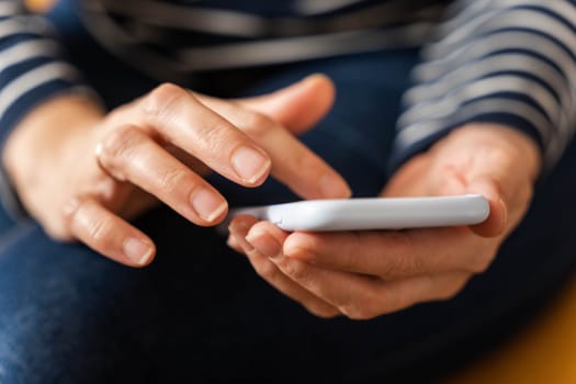 a girl sits on a yellow sofa in casual clothes and skillfully interacts with a smartphone, staying connected and in the information flow.