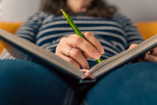 unrecognizable woman writes notes with a pen in a notepad. She thought while sitting on the sofa. Entries in the diary. Entries in a personal diary. the girl concentrated to catch every thought, inspiration or new idea.