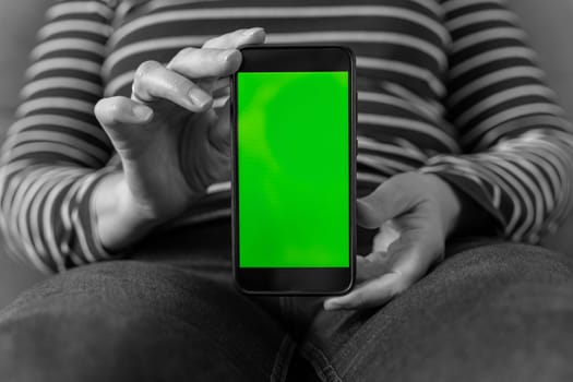 black and white image of unrecognizable woman holding and showing black mobile phone with blank screen mockup. green blank smartphone screen. space for advertising and copying. vertical phone arrangement