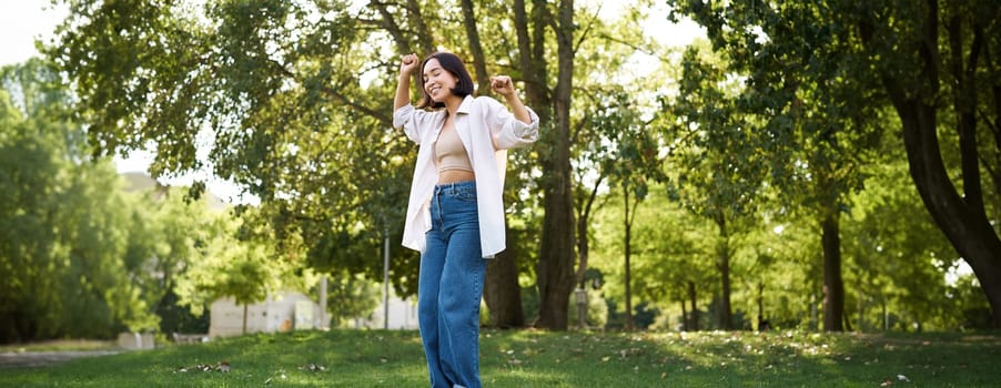 Happy people. Carefree asian girl dancing and enjoying the walk in park, feeling happiness and joy, triumphing.