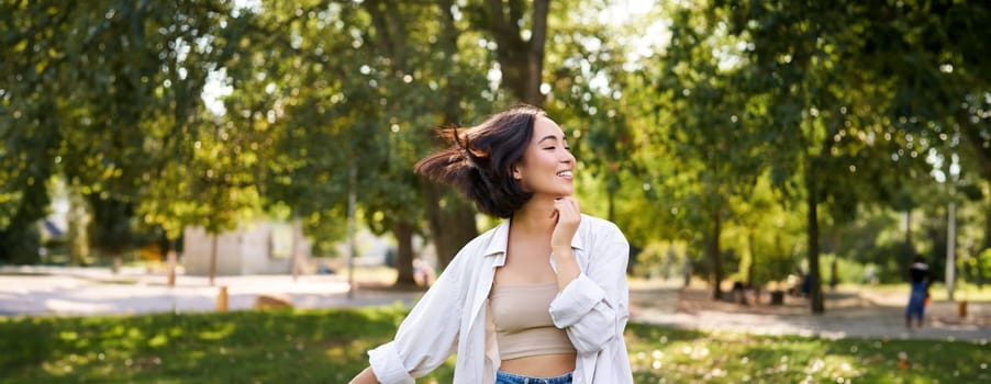 Portrait of carefree young asian woman dancing in park alone, enjoying freedom, smiling with joy. Copy space