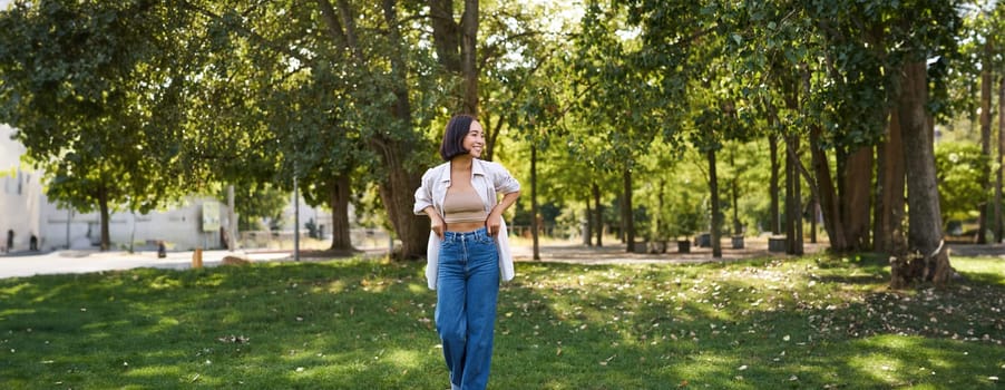 Happy asian girl walking in park, feeling freedom and joy, walking outdoors on sunny day.