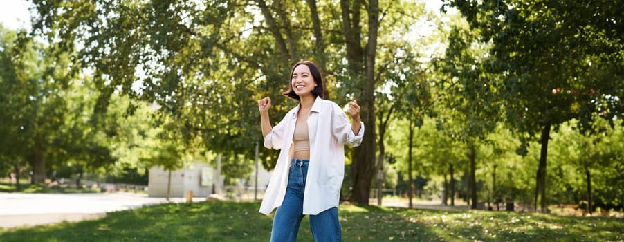 Portrait of happy girl dancing and looking happy, posing in park, enjoying herself, walking alone, feeling freedom and excitement.